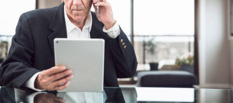 Close up man talking mobile phone looking digital tablet office